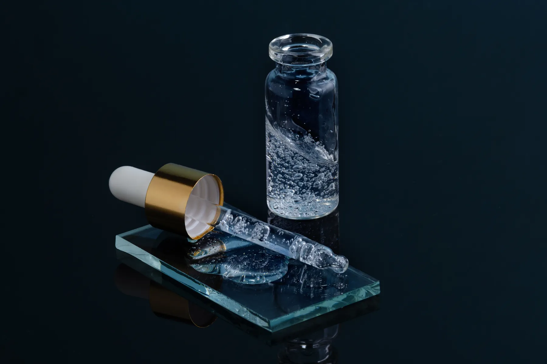 A glass dropper and hyaluronic acid serum on a dark surface